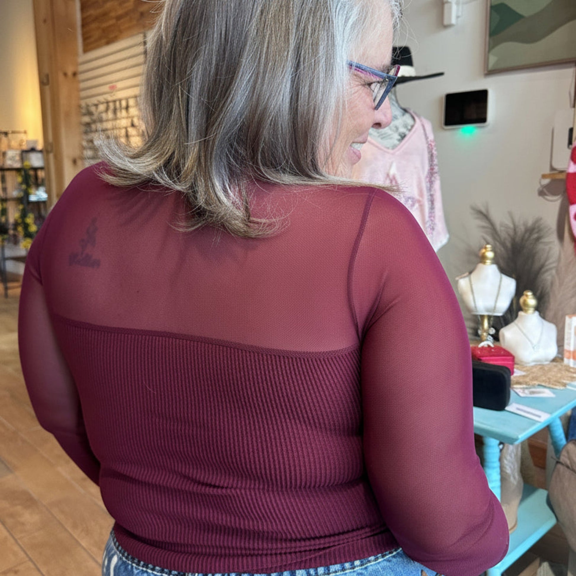 The Sheer Aura Sweetheart top in burgundy, showing the back view with mesh detail and sheer sleeve detail on model at Gypsy Spirit Boutique.