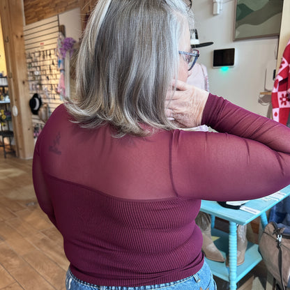 The sheer aura sweetheart top in burgundy, showing the back view mesh detailing and sheer sleeve detail and movement on model at Gypsy Spirit Boutique.